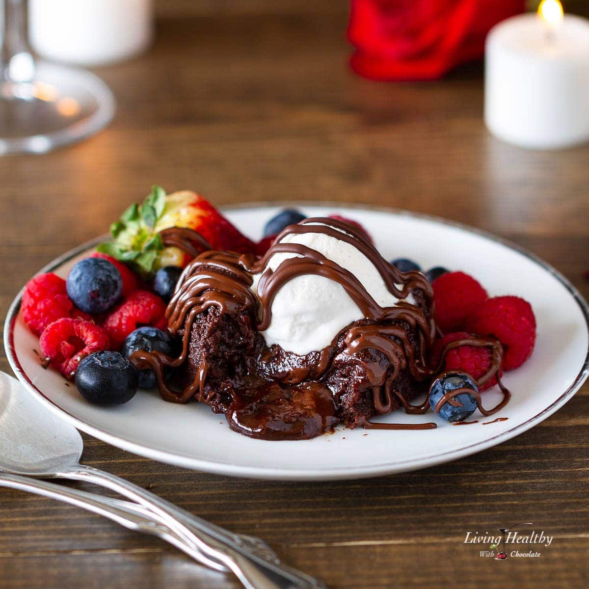A plate with a molten lava brownie topped with whipped cream and chocolate sauce and berries surrounding the brownie