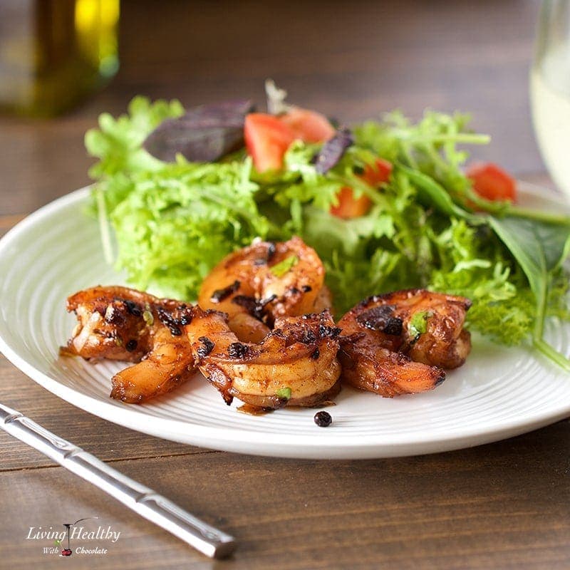 plate of cracked pepper shrimp and salad on wooden table with fork