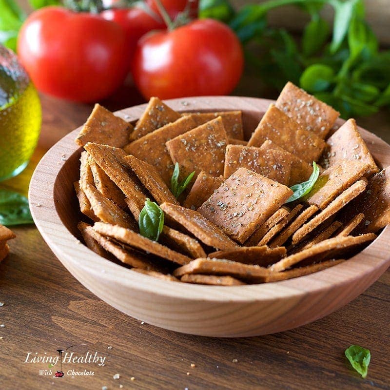 a table with cassava crackers in a wooden bowl with basil leaves, tomato and a jar of oil